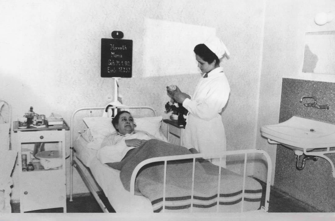 Krankenhaus (Spitalgasse / heute Dr.-Emmerich-Gyenge-Platz): Schwesternschülerin Monika Steurer (geb. Amtmann. *1943/+2020) am Krankenbett von Maria Horvath