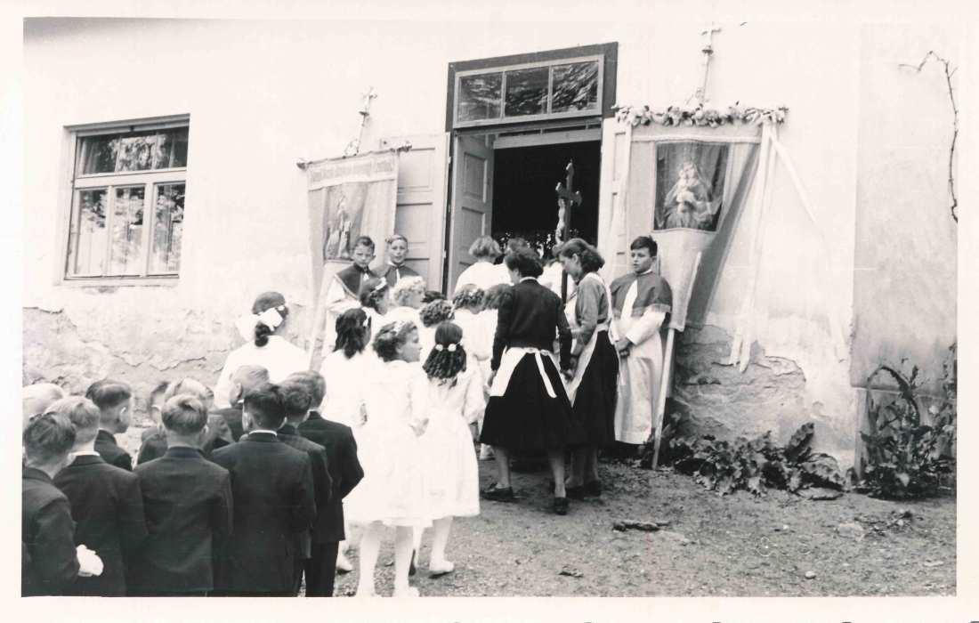 Röm. kath. Pfarre: Hl. Erstkommunion - die Kirchenfahnen und die Ministranten empfangen die Kinder vor dem Pfarrheim